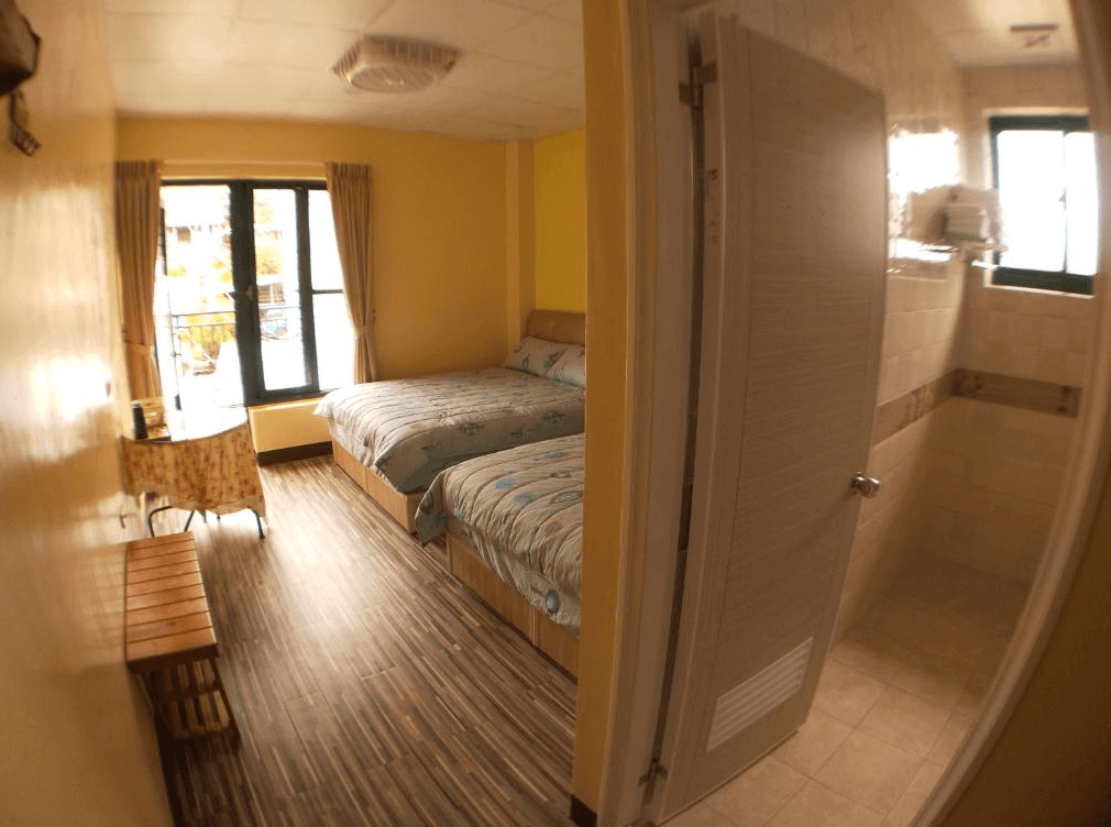 【司馬庫斯住宿】崗好山莊的雙人床的客房，牆面為明亮的黃色，搭配木質地板和簡約家具，窗外可見陽光充足的陽台，房內還設有帶窗的衛浴空間，整體環境溫暖且舒適。