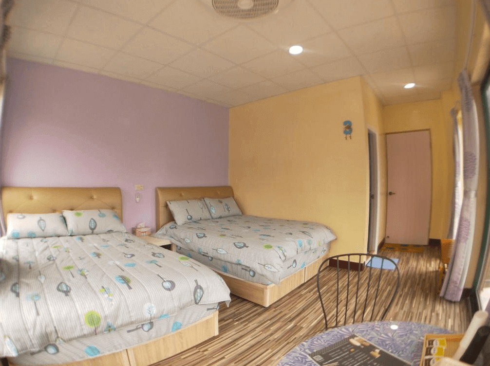 【司馬庫斯住宿】崗好山莊的雙人房，擁有淡紫色和黃色牆面設計，搭配印有葉子圖案的床單，房內設有小桌椅和窗簾，光線充足，整體氛圍清新且溫馨。