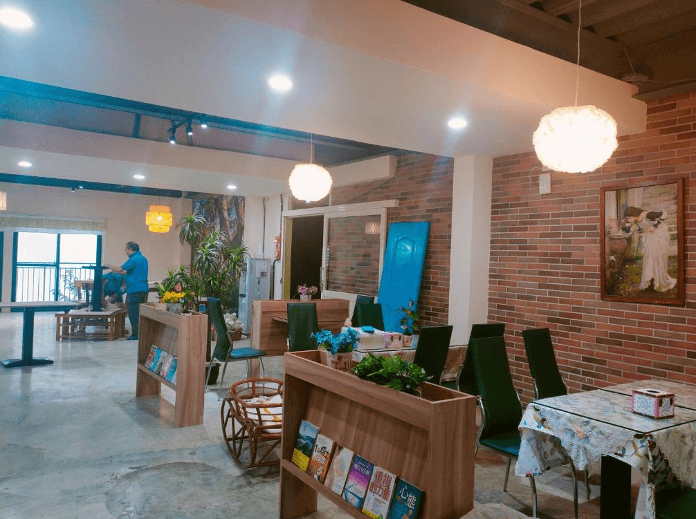【司馬庫斯住宿】崗好山莊的餐廳內部的另一視角，牆面以紅磚設計，擺放有綠色植物與裝飾畫，桌椅風格多樣，增添了溫馨與生機的氛圍，適合放鬆和交流的場所。