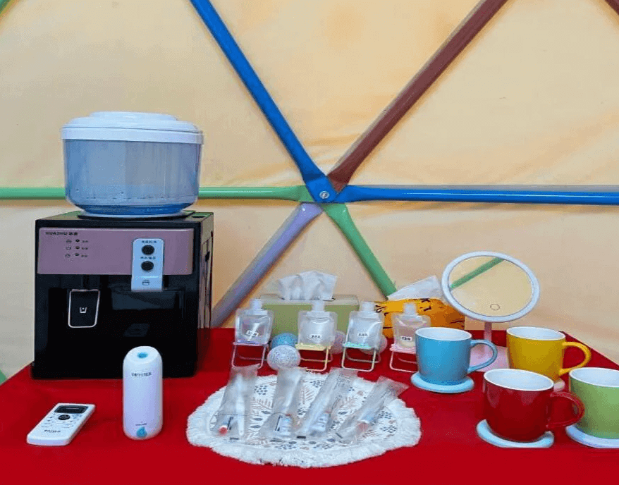 【司馬庫斯住宿】悠野_s露營區的帳篷內的一個紅色桌面，擺放著飲水機、各式小瓶盥洗用品、彩色馬克杯和小鏡子，用品分類整齊，營造出方便與溫馨的氛圍。