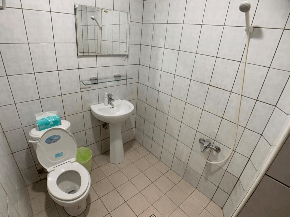 【新竹火車站住宿】懶骨頭 Lazy Bone的浴室採用白色瓷磚設計，牆面與地板的瓷磚紋理統一，乾淨整潔。內設馬桶、洗手台和淋浴設備，空間雖小但功能齊全，注重實用性。