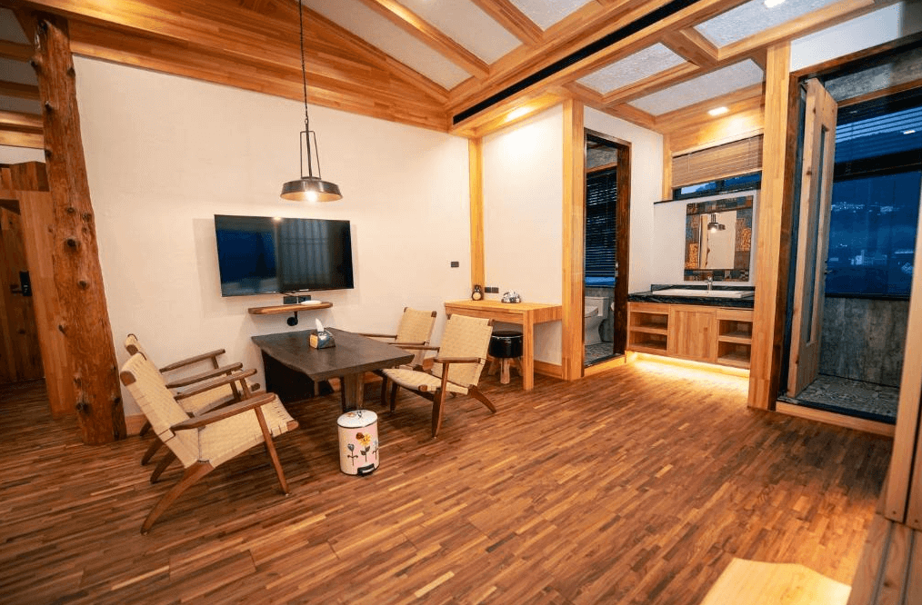 【阿里山住宿】找茶人家-檜木民宿的檜木結構會客區設有簡約木桌椅與吊燈，牆面掛有電視，營造舒適的休憩環境。開放式空間與精緻的洗手台設計，增添便利性與現代感。