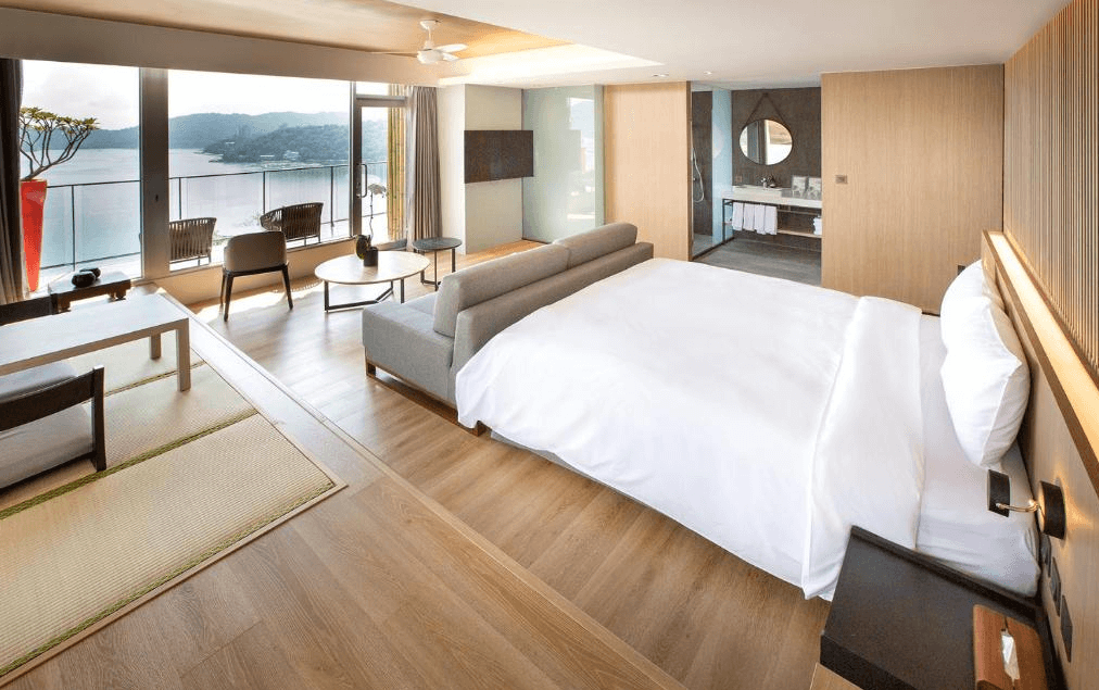 【日月潭住宿】承億文旅 潭日月的房間採用現代簡約風設計，大片落地窗提供寬廣湖景視野，木質地板與傢俱搭配柔和燈光，營造溫馨舒適的氛圍。寢區與客廳區分隔明確，讓空間更具功能性。