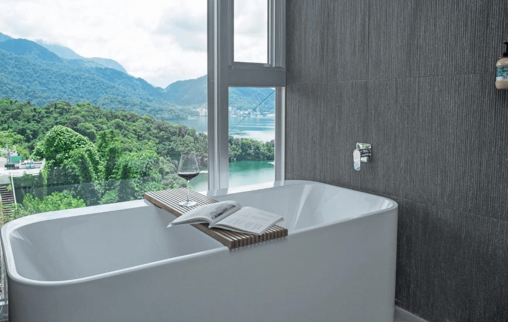 【日月潭住宿】承億文旅 潭日月的浴室配備獨立式白色浴缸，設計高雅且實用。窗外山水景致美不勝收，讓住客在沐浴時也能感受身心放鬆。牆面採用深灰色瓷磚，增添現代質感。
