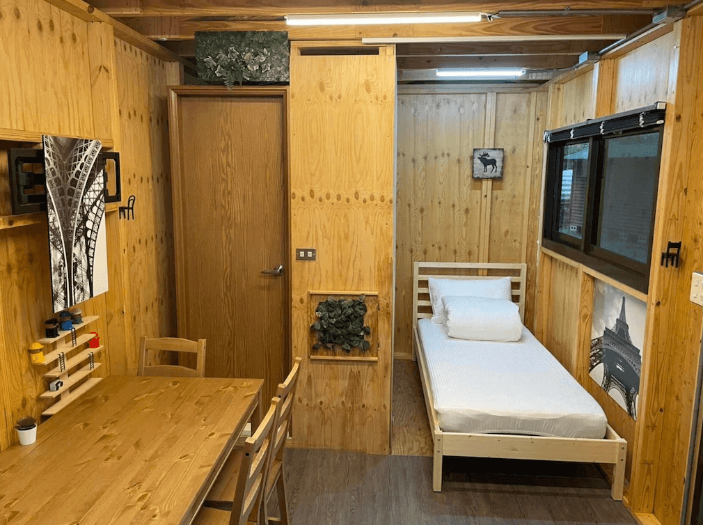 【司馬庫斯住宿】拾階莊園（內灣露營車）的雙床房，兩張雙人床設有木質床頭與白色寢具，床尾擺放黑色皮革行李凳，房間採用木質和簡約設計，牆頂有條紋式天花板，整體呈現溫暖的居家感。