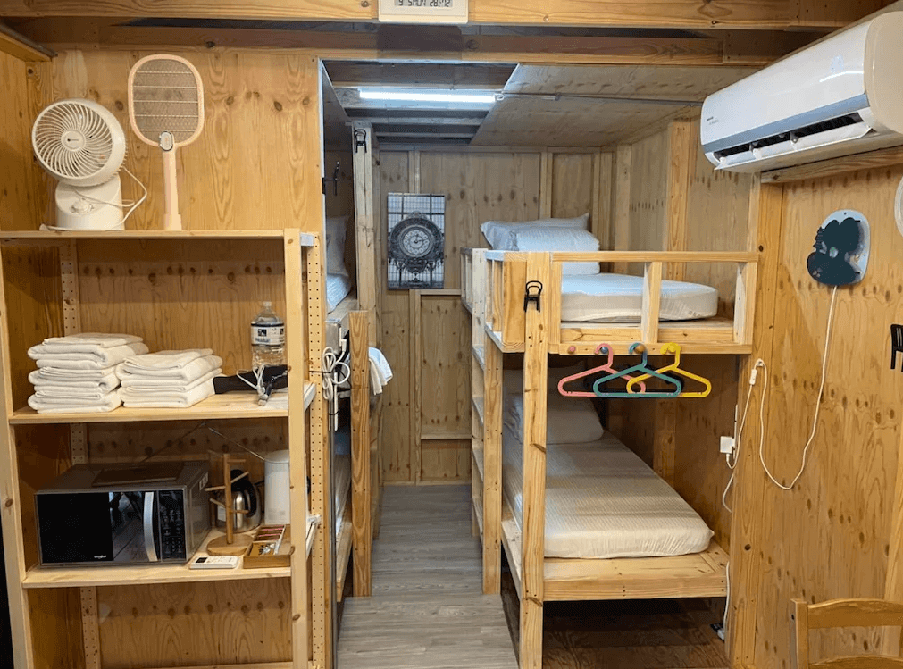 【司馬庫斯住宿】拾階莊園（內灣露營車）的現代化客房，配備一張大床與白色床頭，房內有木質托盤與滾輪置物架，窗外景色自然，地板採用灰色設計，營造出清新與舒適的氛圍。