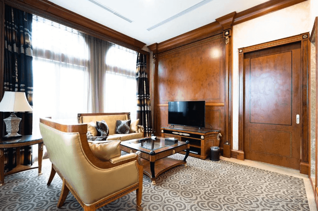 【新竹火車站住宿】新舍商旅新竹館的客廳內設有金色調沙發與木質家具，整體風格古典高雅。大片窗戶採用透光窗簾，讓空間明亮且溫暖。木質牆面與細緻的裝飾細節突顯出豪華與品味。