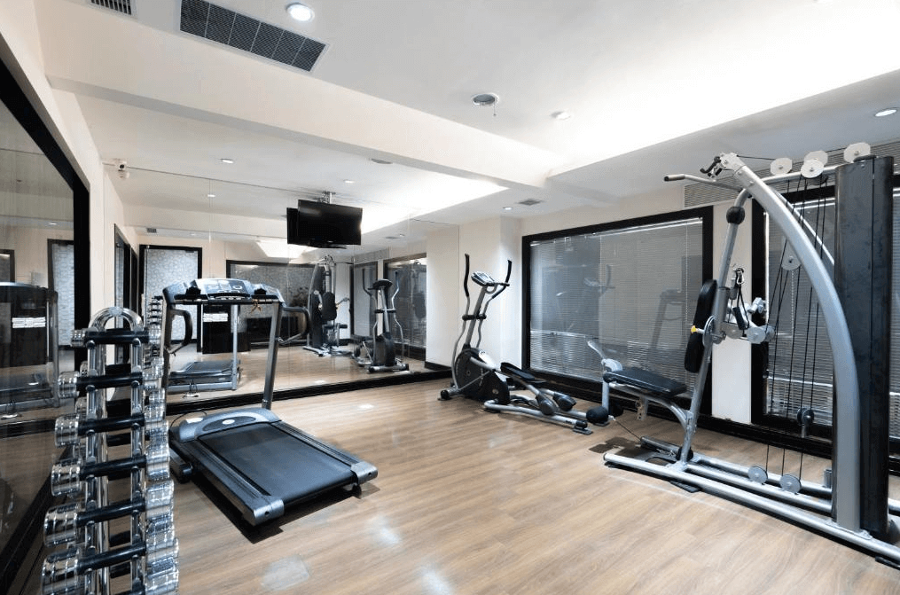 【新竹火車站住宿】新舍商旅新竹館的健身房內設有跑步機、健身車和多功能訓練器材，並配有一排啞鈴。室內採用木質地板與鏡面牆設計，增加空間感並提升鍛煉體驗。窗外透入自然光線，讓健身環境更加明亮舒適。