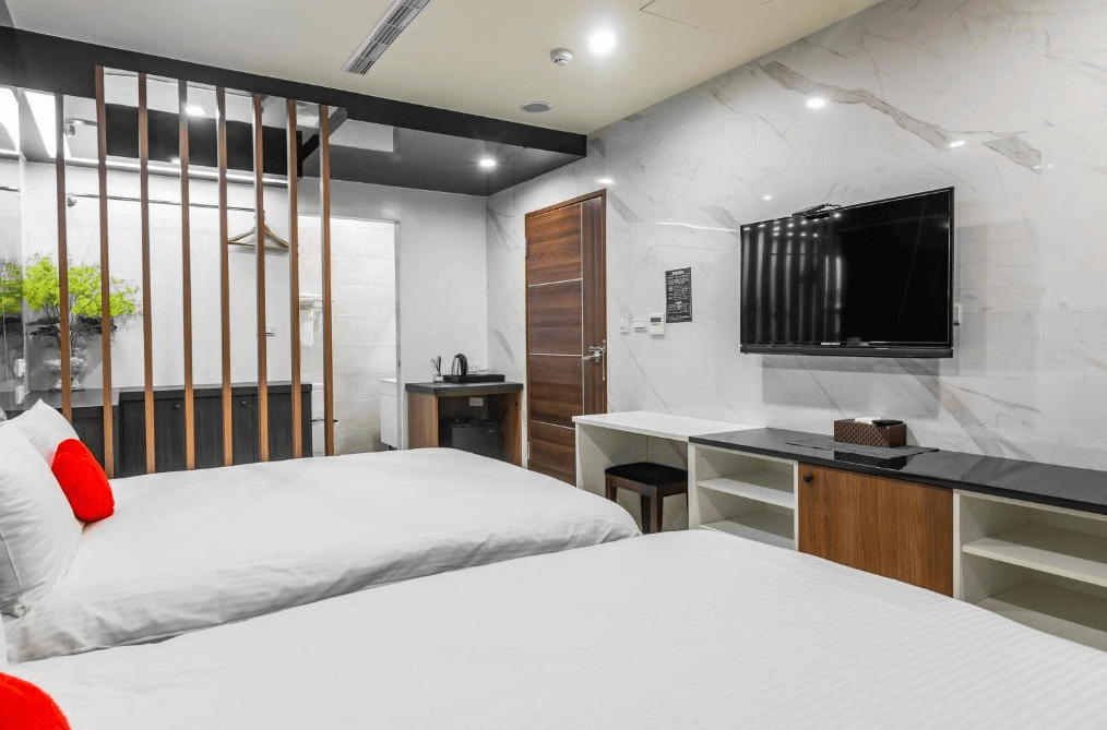 【日月潭住宿】日月潭兒茶宿的房間內部採用木質與大理石紋的混搭設計，配以木條屏風分隔空間，創造出層次感。設有雙人床、電視以及整潔的收納櫃，並搭配紅唇抱枕作為點綴，營造舒適的住宿氛圍。