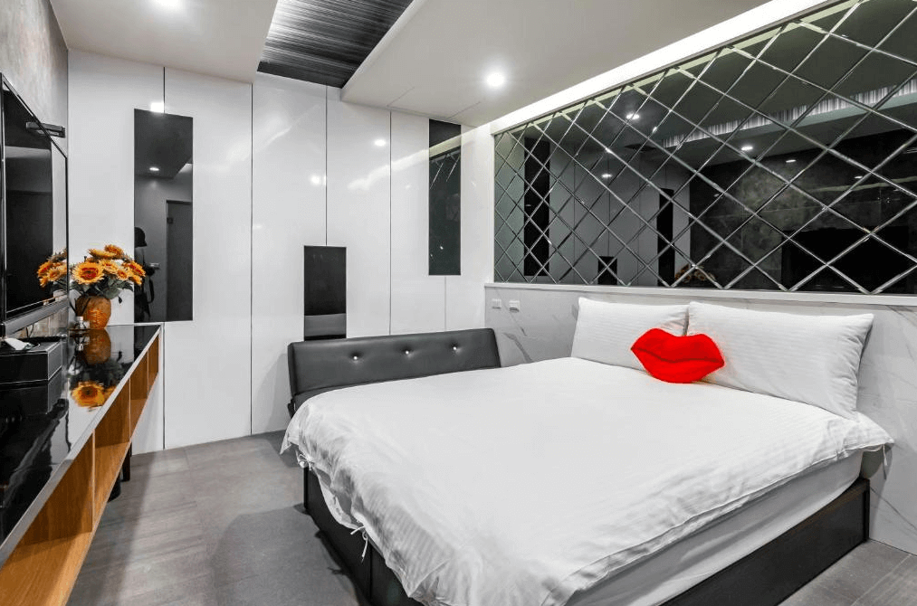 【日月潭住宿】日月潭兒茶宿以白色大理石紋與鏡面牆搭配，房間呈現簡潔又具奢華感的設計。床頭後方的鏡面拼接設計增添空間感，配以紅唇抱枕點綴。房間內設有沙發與置物空間，提升實用性與舒適度。