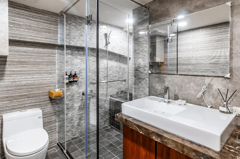 【日月潭住宿】日月潭兒茶宿的浴室採用現代化設計，牆面以條紋與幾何紋理拼貼瓷磚呈現質感，乾濕分離的淋浴空間設計，配備多款高級洗浴用品。洗手台採用大理石台面，搭配明亮鏡面，展現細膩設計與實用功能的結合。