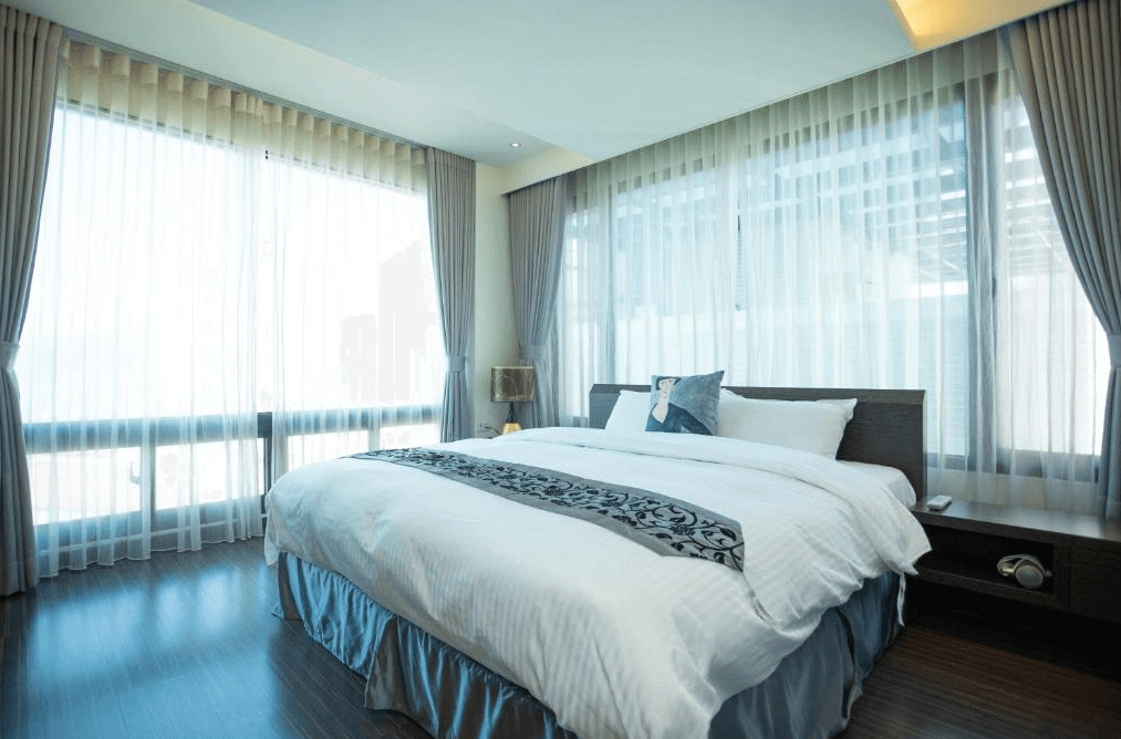 【日月潭住宿】日月潭天月水色民宿的房間採光極佳，三面落地窗設計讓自然光充滿室內。床鋪以簡潔的白色寢具搭配素雅花紋床尾巾，呈現現代簡約風格，窗外景色一覽無遺，讓住客享受視覺上的開闊感。