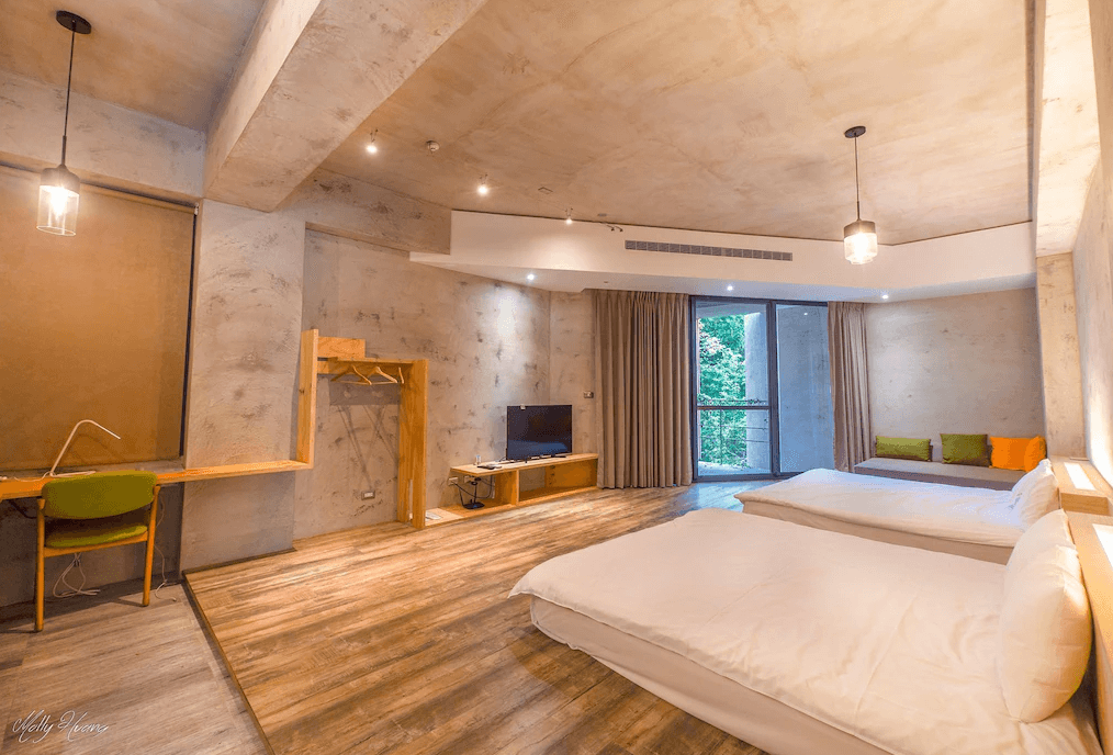 【日月潭住宿】日月潭山慕藝旅寬敞的家庭房間內部空間感十足，地板為溫暖木質材質，牆面延續清水模的現代設計。雙大床設計適合家庭或團體入住，房內設有工作桌、掛衣空間與電視，並配有大片玻璃門，讓自然光線充足。