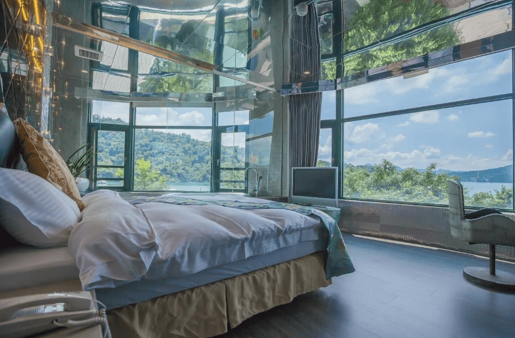 【日月潭住宿】日月潭水岸休閒飯店的房間，床位於大幅落地窗旁，窗外可欣賞湖景，天花板有特殊的鏡面裝飾，展現現代奢華感。