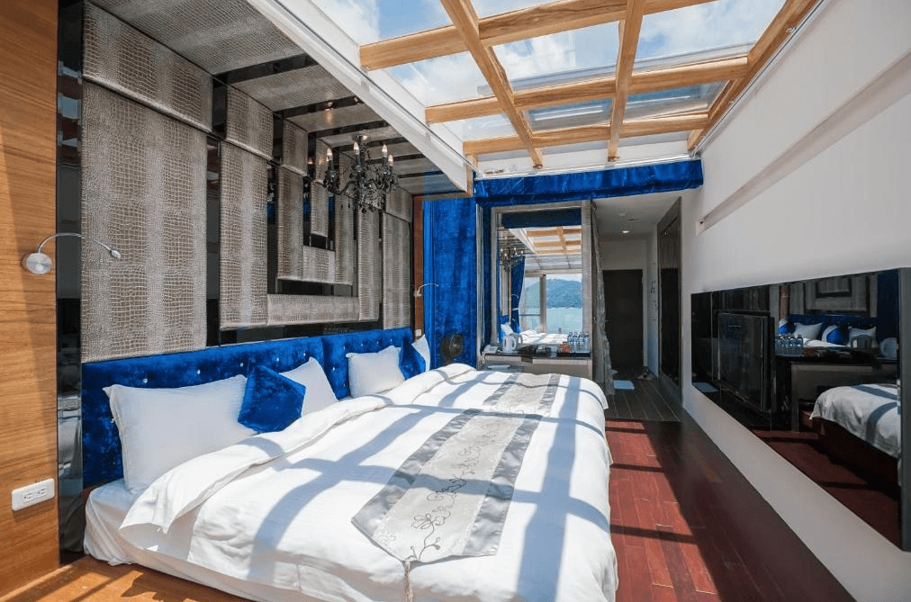 【日月潭住宿】日月潭水岸休閒飯店以深藍色與木質為主題的房間，床頭設有鏡面牆，天花板為透明玻璃，陽光灑入室內，氛圍明亮典雅。