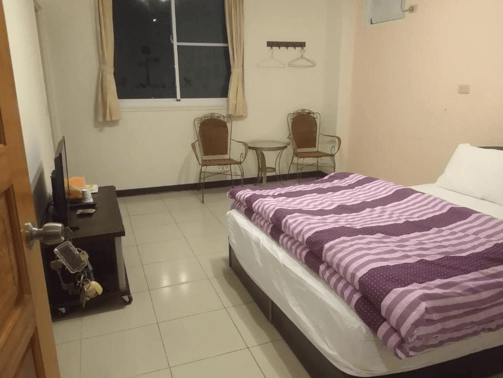 【司馬庫斯住宿】星光流域咖啡民宿的客房，內部配有雙人床、紫色條紋床單，牆角設有兩張鐵藝椅子和小圓桌，窗外為夜間景色，房內設計溫馨且實用。