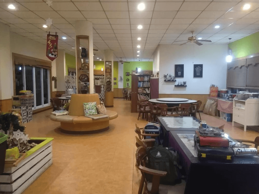 【司馬庫斯住宿】星光流域咖啡民宿的公共空間，設有圓形沙發座椅區、木製餐桌和書櫃，牆上裝飾有綠植與藝術畫，環境明亮且充滿家庭式的溫暖氛圍。