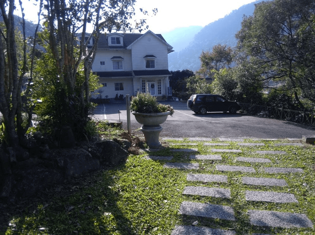 【司馬庫斯住宿】星光流域咖啡民宿外部拍攝，一棟白色歐式建築矗立於綠意盎然的庭園中，前方有停車空間與石板小徑，背景為山林景色，環境靜謐且充滿自然氣息。