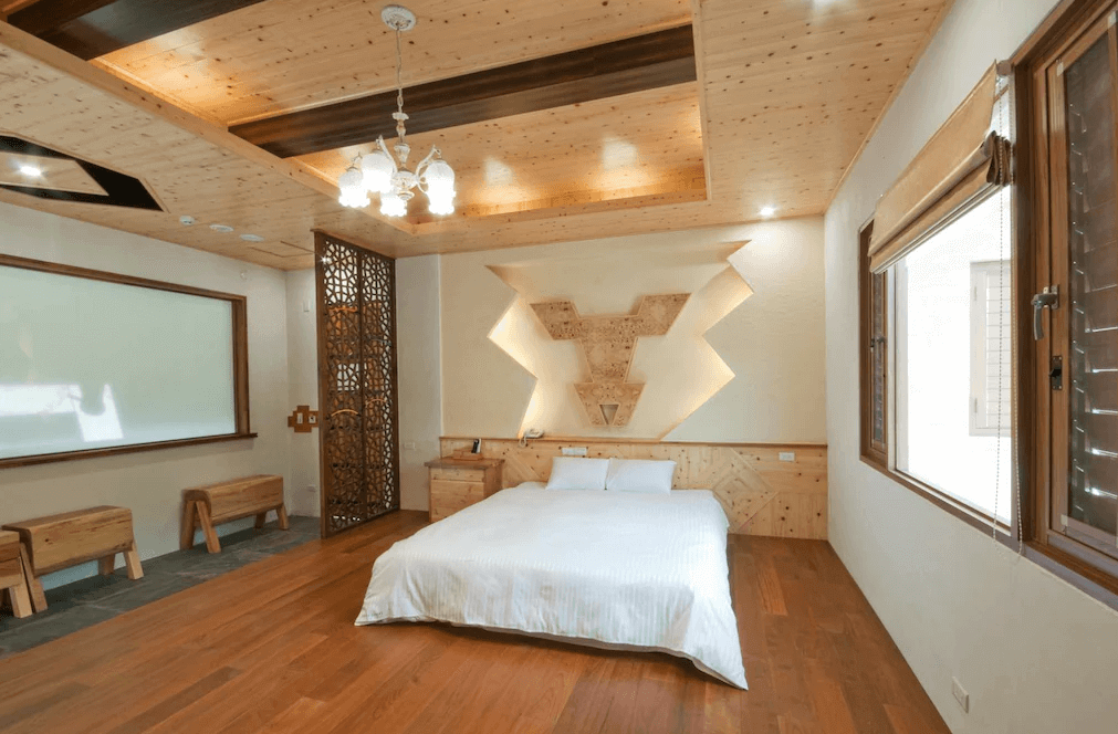 【廬山溫泉】春陽一品居的溫馨木質設計的雙人房，床頭牆上有獨特的木雕裝飾，搭配木質天花板與柔和的燈光，營造出溫暖放鬆的氛圍。窗戶設計簡約，採光良好，房內擺設以木質家具為主，展現自然風格。