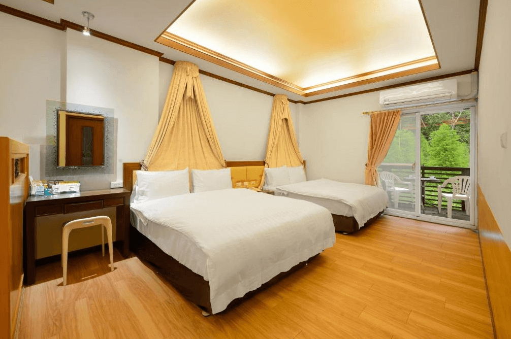 【司馬庫斯住宿】會來尖石溫泉渡假村的雙床房，設有兩張大床，床頭頂部掛有金色帷幔，窗外連接陽台可欣賞戶外景色，室內採用木質地板與暖色調燈光，空間明亮舒適。