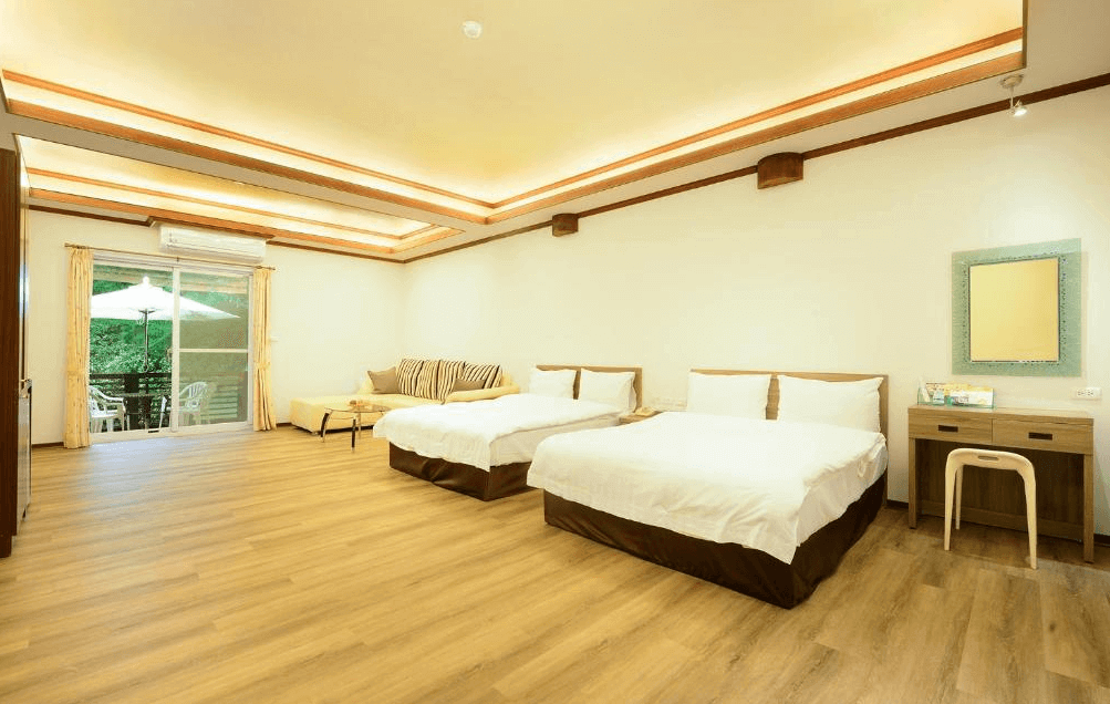 【司馬庫斯住宿】會來尖石溫泉渡假村的四人房，內設兩張大床與一組木質沙發，窗外通向陽台，室內裝潢簡約，採用木地板與天花板間接照明，呈現舒適又大氣的居住環境。