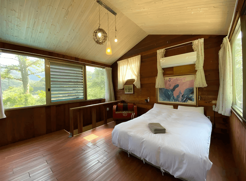 【廬山溫泉】森之秘湯的溫馨木質設計的雙人房，床頭牆上有獨特的木雕裝飾，搭配木質天花板與柔和的燈光，營造出溫暖放鬆的氛圍。窗戶設計簡約，採光良好，房內擺設以木質家具為主，展現自然風格。