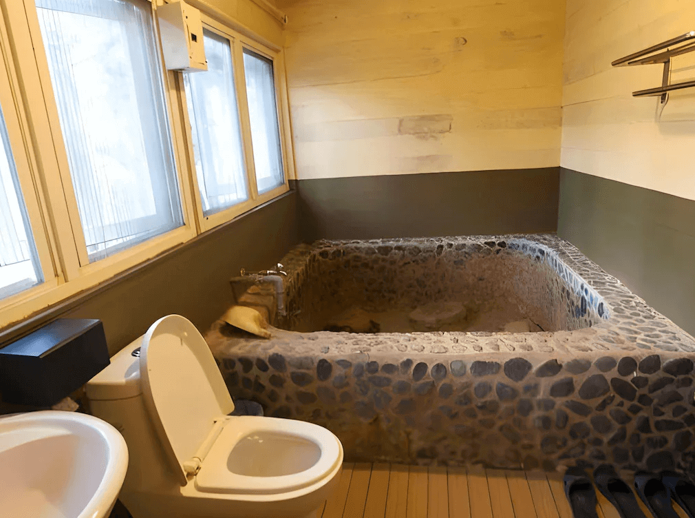 森之秘湯的座落於群山環繞中的兩層樓建築，外觀簡約大氣，白色與米色調的外牆搭配對稱窗戶設計，散發典雅氛圍。前方為寬敞的停車空間，周圍被綠意盎然的山景環抱，展現寧靜悠閒的自然環境。