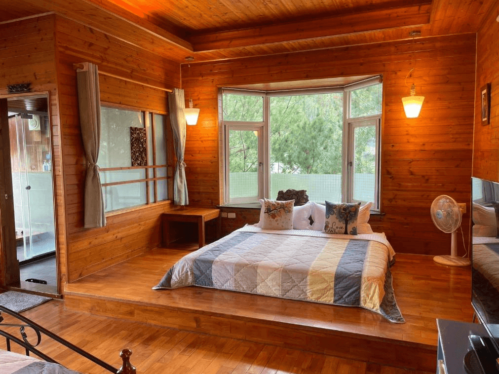 【埔里住宿】水月山莊的木屋客房，中央設有一張加大的床，窗外能欣賞到綠意盎然的庭院景色，室內以木材裝潢為主，燈光柔和溫暖，提供舒適的住宿體驗。