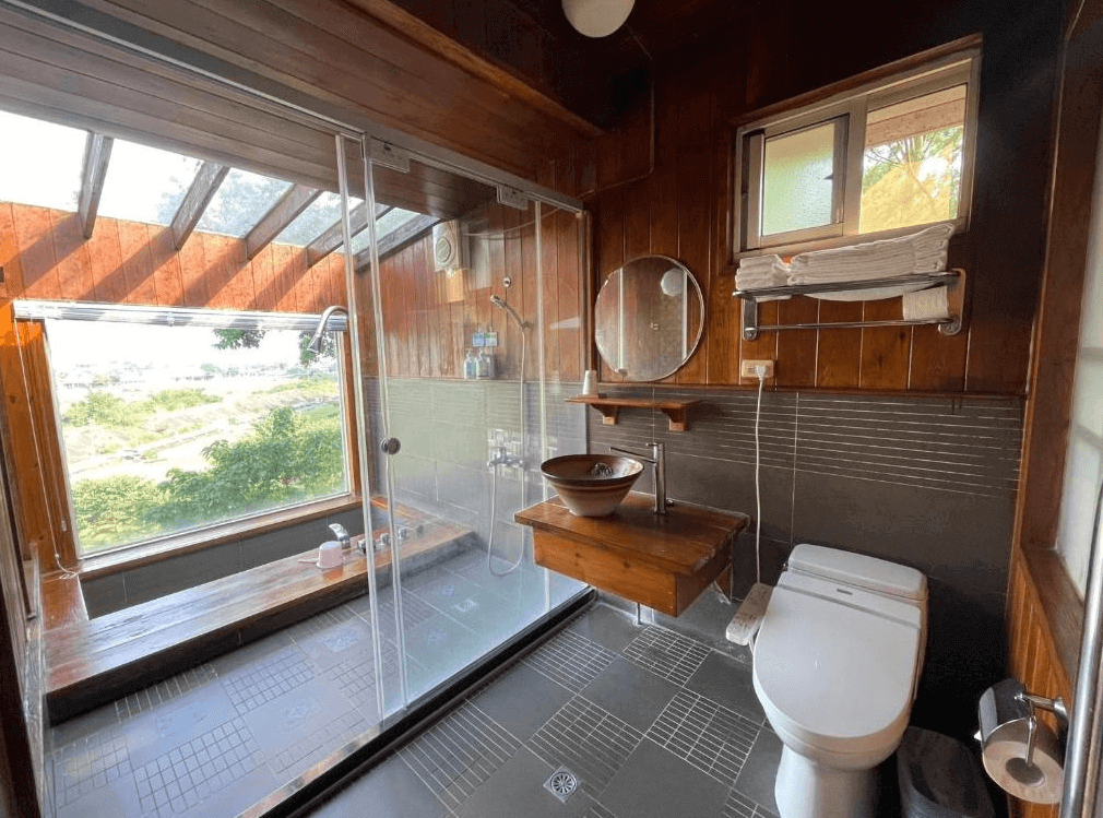 【埔里住宿】水月山莊的木質設計的浴室，設有玻璃淋浴間，旁邊是帶景觀窗的浴缸，窗外可見大自然的景色，整體採光明亮，帶有濃厚的自然風格。