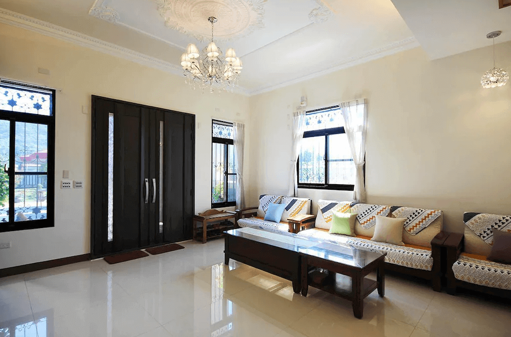 【埔里住宿】水部子山莊民宿的公共客廳，設有長沙發與多彩抱枕，牆面大窗戶讓光線充足。中央擺放木質茶几，天花板裝飾著華麗的水晶吊燈，展現典雅風格。