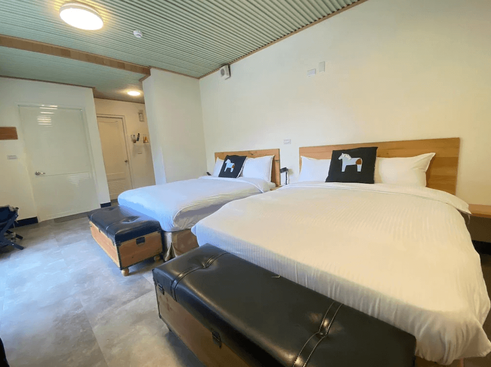 【司馬庫斯住宿】湯迴廊秀巒的雙床房，兩張雙人床設有木質床頭與白色寢具，床尾擺放黑色皮革行李凳，房間採用木質和簡約設計，牆頂有條紋式天花板，整體呈現溫暖的居家感。