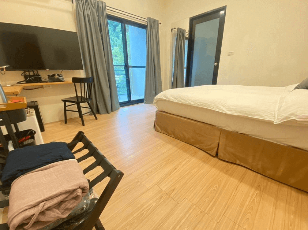 【司馬庫斯住宿】湯迴廊秀巒的雙人房，床上鋪有潔白的寢具，房間內設有平板電視、簡約書桌與椅子，推拉玻璃門通往陽台，光線明亮，窗簾為灰色，地板採用木紋設計。