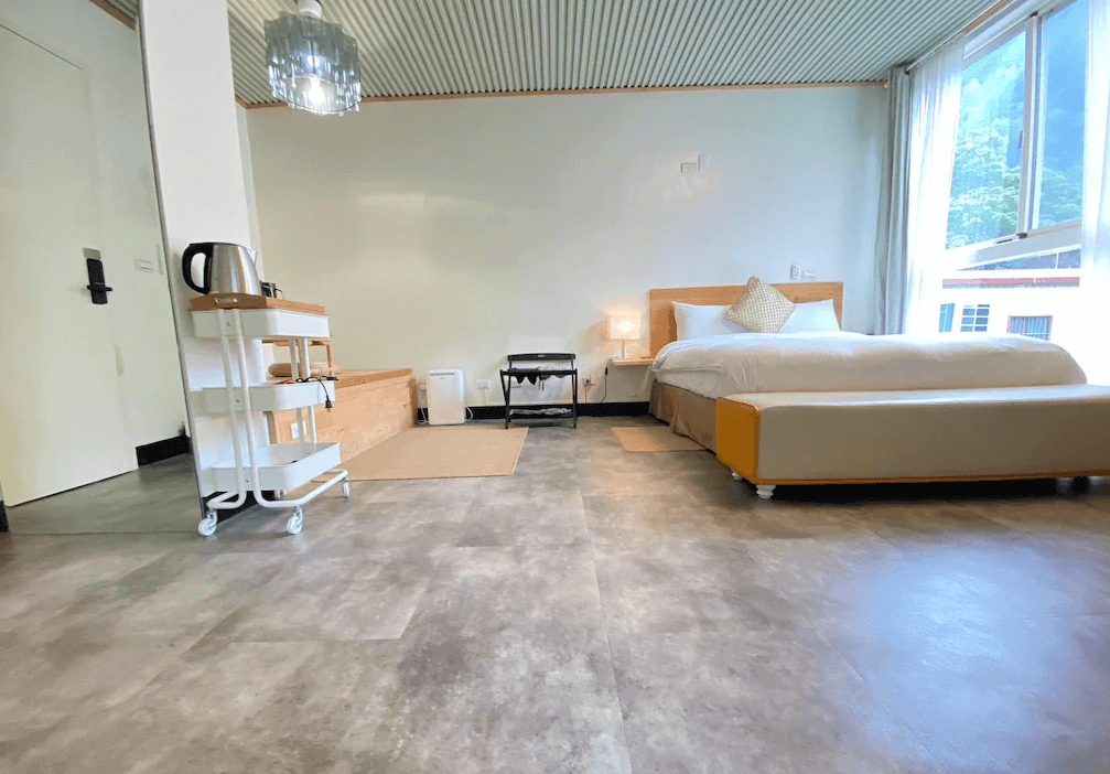 【司馬庫斯住宿】湯迴廊秀巒的現代化客房，配備一張大床與白色床頭，房內有木質托盤與滾輪置物架，窗外景色自然，地板採用灰色設計，營造出清新與舒適的氛圍。