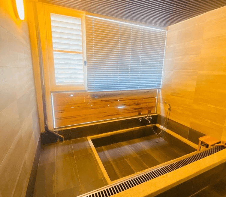 【司馬庫斯住宿】湯迴廊秀巒的湯室，設有木質和石材組合的浴池與洗浴設備，牆面與天花板採用自然木色設計，窗戶配有百葉簾，整體空間明亮溫馨，適合放鬆使用。