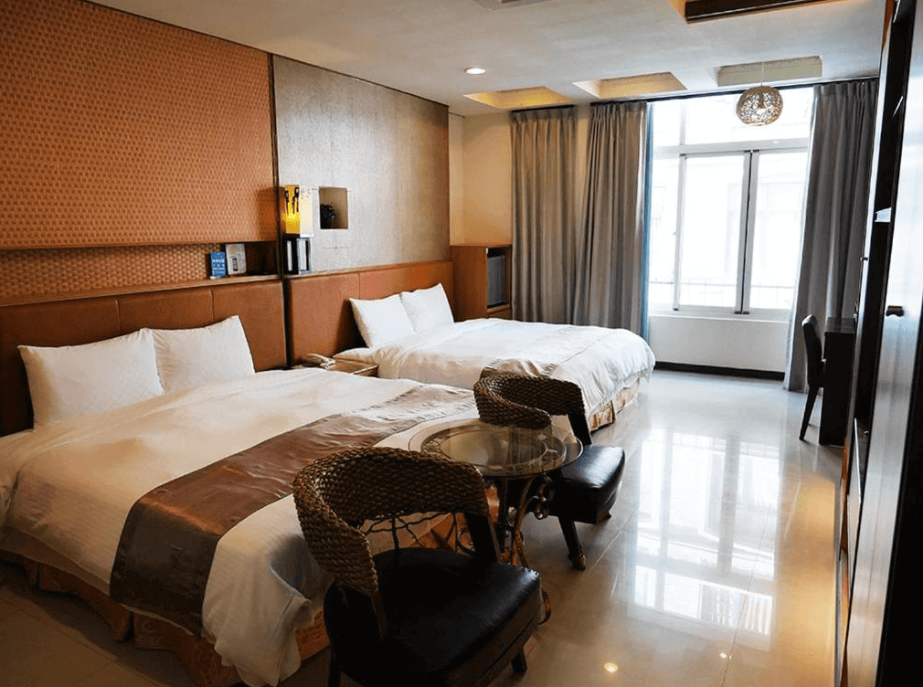 【日月潭住宿】澄園旅店的雙床房型，兩張大床整潔地排列，房內使用暖色調設計，設有編織椅子和小圓桌，窗戶提供明亮的自然採光，適合家庭或朋友共同入住。