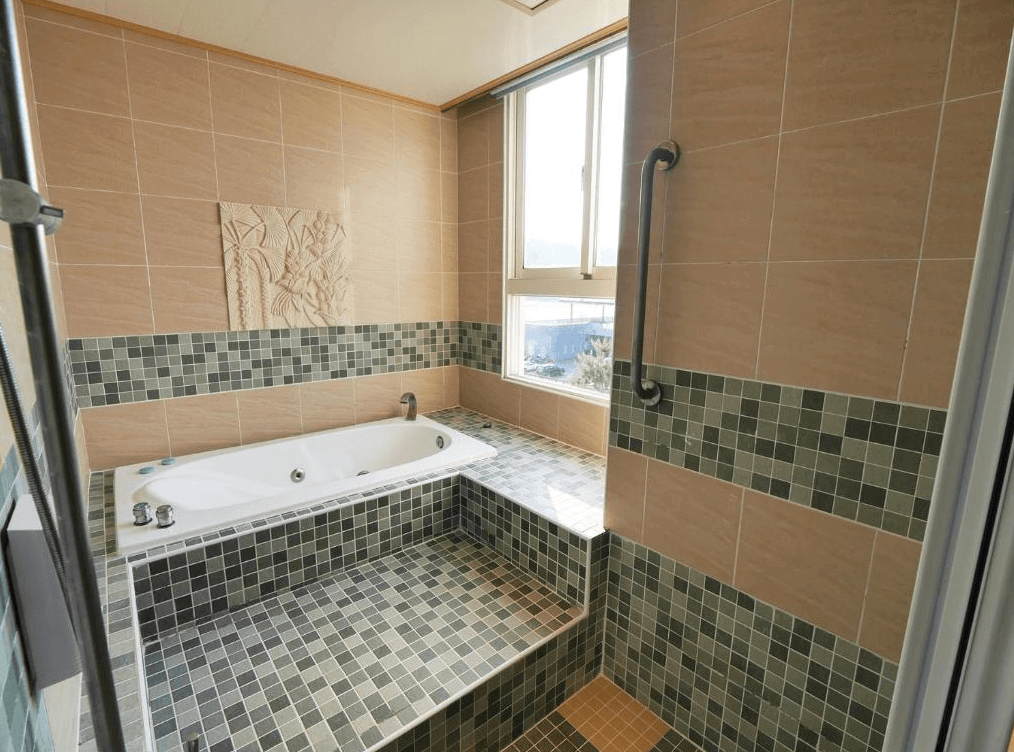 【日月潭住宿】澄園旅店的寬敞的浴室設計，牆面採用米黃色瓷磚搭配馬賽克花紋，提供大浴缸與防滑扶手，窗外能欣賞自然景致，功能性與美觀兼具。