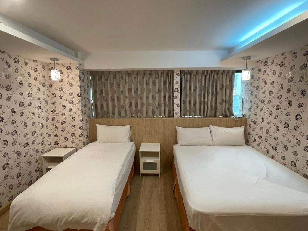 【寧夏夜市住宿】瑾旅南西館的客房，包含一張大雙人床和一張單人床，牆面以花卉壁紙裝飾，搭配溫暖的燈光，窗簾遮擋部分自然光。