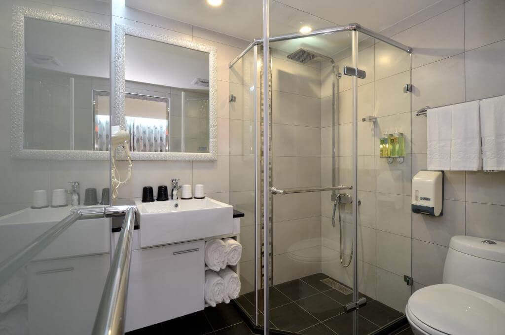 【寧夏夜市住宿】瑾旅南西館的浴室設計，配有玻璃淋浴間、白色洗手台和大面鏡子，整潔明亮，牆面為簡約風格的淺灰色瓷磚。