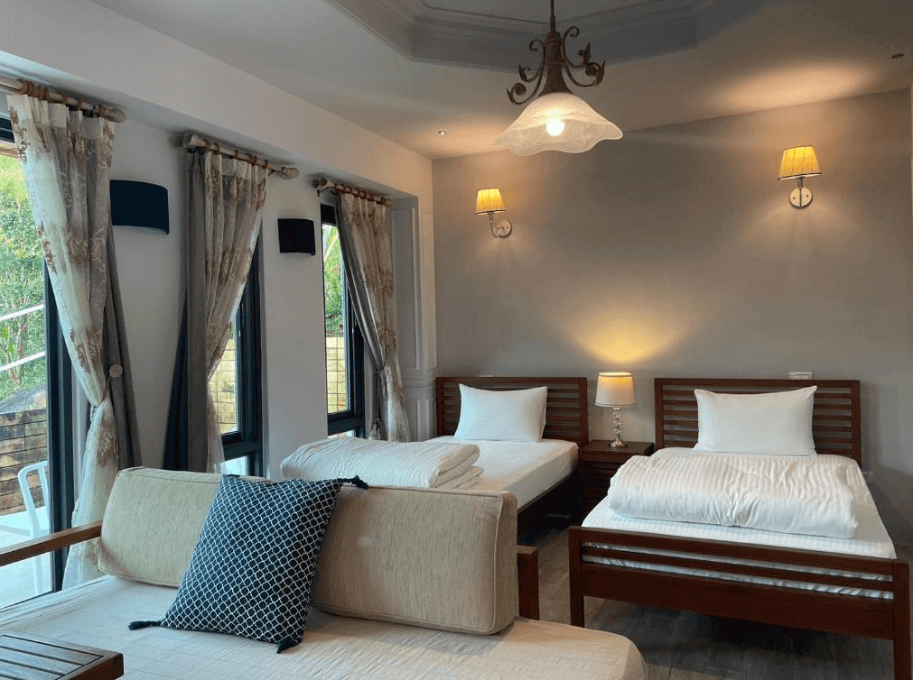 【埔里住宿】白舍·青丘的雙床房，擺設兩張木質床架，搭配白色床單，牆面採用柔和的米灰色。房間設有多扇窗戶，窗簾是蕾絲與花紋的搭配，提供充足自然光，整體感覺溫暖且典雅。