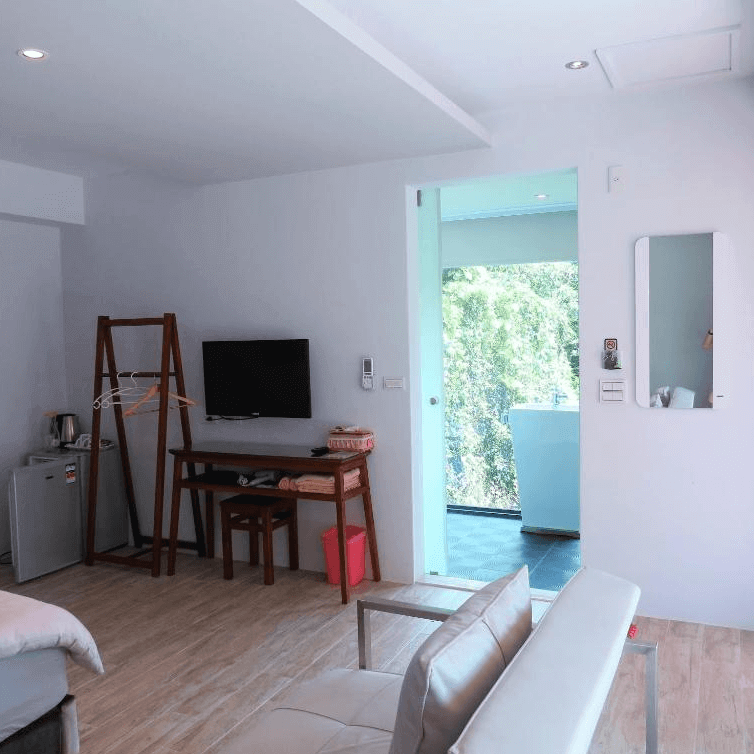 【埔里住宿】白舍·青丘設備齊全的客房，內有木質書桌、小型冰箱與電視，還設有一個可掛衣物的木質衣架。房間延續簡約風格，窗外綠意盎然，空間乾淨且實用。