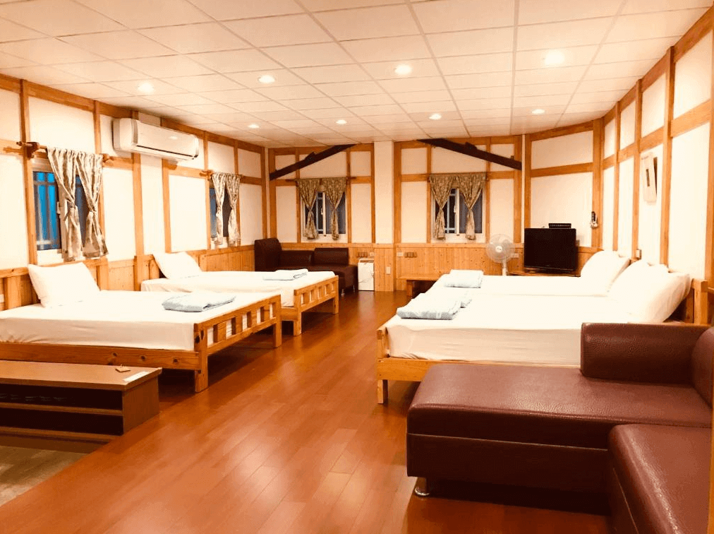 【嘉義寵物友善住宿】竹崎白樹腳驛棧的多人房，內部設有多張木製單人床，牆面採用木框與白牆結合的設計，地板為木質，房間內有沙發、電視與窗簾，整體感覺溫暖而實用。