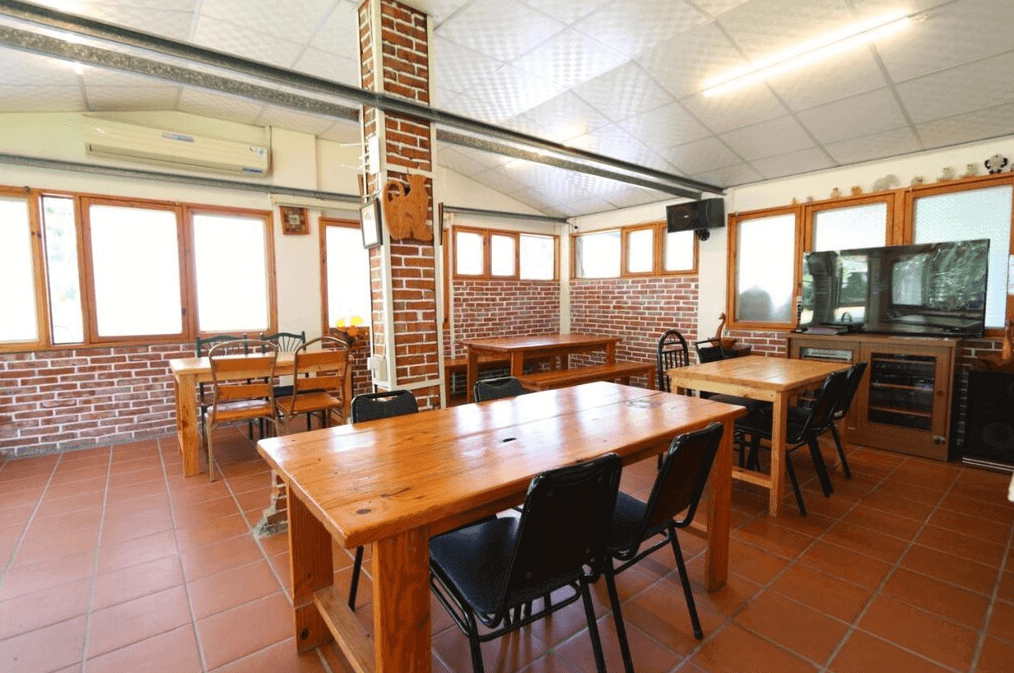 【嘉義寵物友善住宿】竹崎白樹腳驛棧的公共用餐空間，內部以紅磚牆和大窗設計，擺放多張木製桌椅，地板為紅磚鋪設，環境明亮且寬敞，適合團體聚會或用餐。