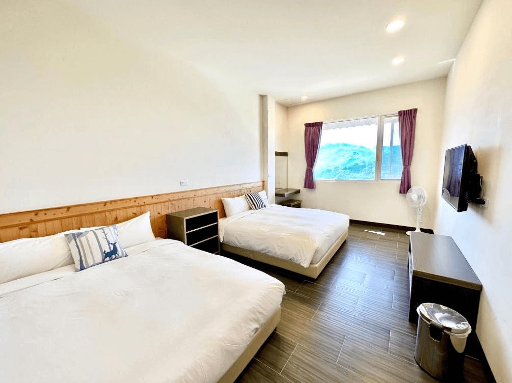 【阿里山住宿】紫龍星空民宿寬敞的客房內配置簡約，設有兩張大床，搭配白色牆面與木質裝飾，營造出清新簡潔的氛圍。窗外風景優美，讓住客享受自然光與寧靜的環境。