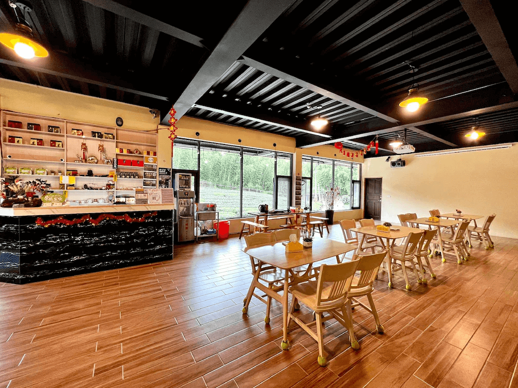 【阿里山住宿】紫龍星空民宿的餐廳空間設計寬敞明亮，擁有大片玻璃窗，讓室外自然景致融入室內。桌椅擺設整齊，適合用餐或舉行小型活動，前方櫃檯提供茶飲與紀念品。