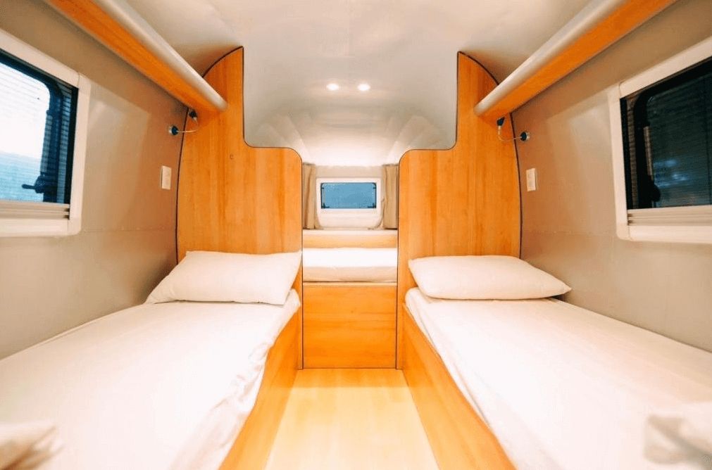【埔里住宿】緣溪行森林營地的露營車內部，設有兩張單人床，中央是木質裝飾的隔間，牆面與天花板採用簡約現代風格設計，側邊窗戶提供自然採光，空間小巧而舒適。