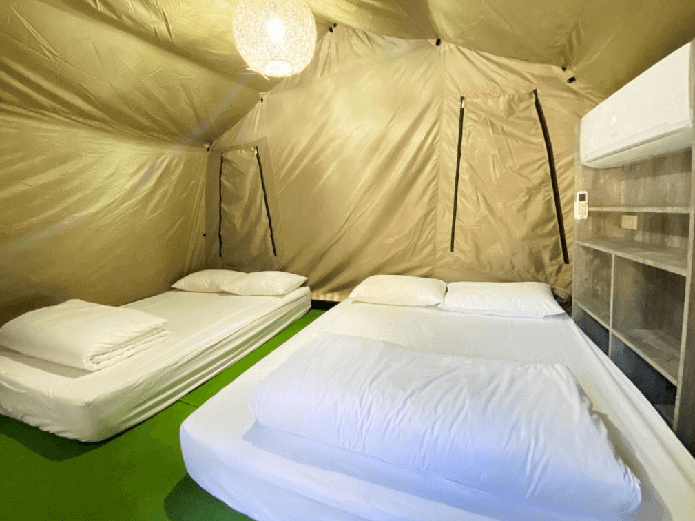 【埔里住宿】緣溪行森林營地的帳篷內部，鋪設兩張雙人床，床鋪整齊地鋪著白色床單與枕頭，帳篷內配有空調與吊燈，提供簡單卻舒適的露營體驗。