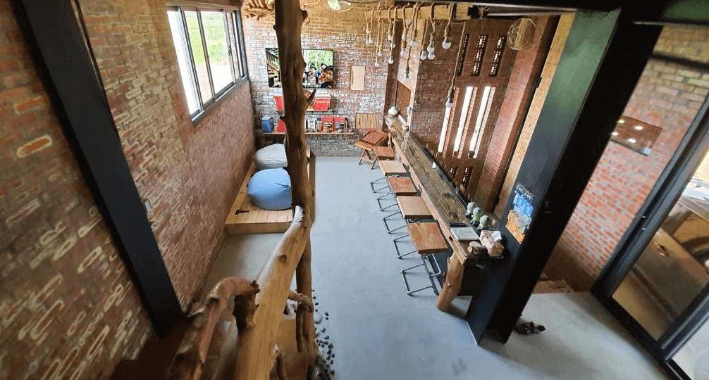 【埔里住宿】缽割貓點點紅磚牆和木材為特色的公共空間，內部設有長桌與多個座椅，旁邊還有豆袋椅和擺設書籍的小空間，適合休憩或交流。整體空間風格溫暖且富有質感。