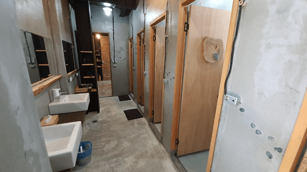 【埔里住宿】缽割貓點點的公共衛浴空間，牆面與地板採用工業風水泥質地設計，設有數個獨立的木門衛浴隔間與簡約洗手台，整體環境乾淨整潔，風格極簡而實用。