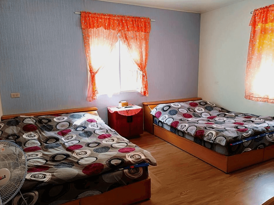 【廬山溫泉】翔婷茶工坊-登坊輕生活的兩張雙人床的房間，以藍色與白色壁紙搭配橘色花邊窗簾，空間明亮寬敞。床鋪擺設簡單，床單帶有圓形幾何圖案，提供舒適的家庭住宿選擇。窗邊擺放小紅色桌櫃，增添復古風格。