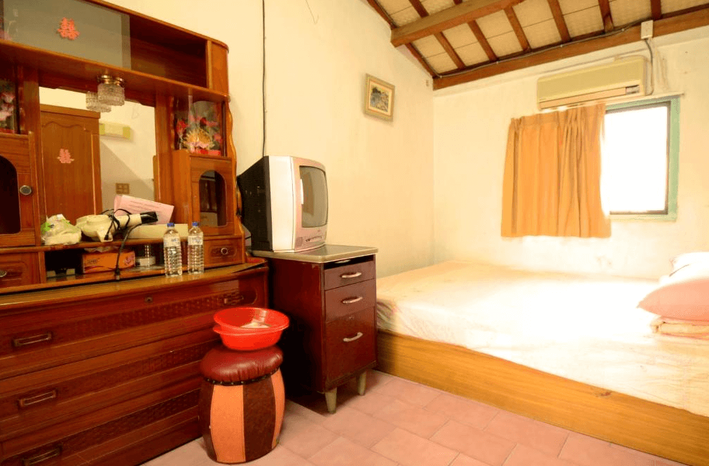 【嘉義寵物友善住宿】船仔頭天賞居民宿復古風格的房間，內部配有木質梳妝台、老式電視和木床，窗邊掛著橘色窗簾，天花板採用斜面木樑設計，整體風格樸素懷舊。